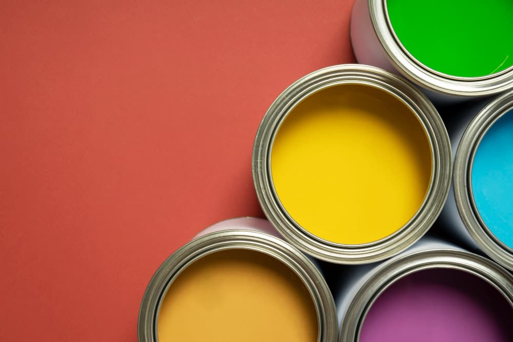 Pots de peinture jaune, verte, bleue et mauve ouverts sur un fond rouge